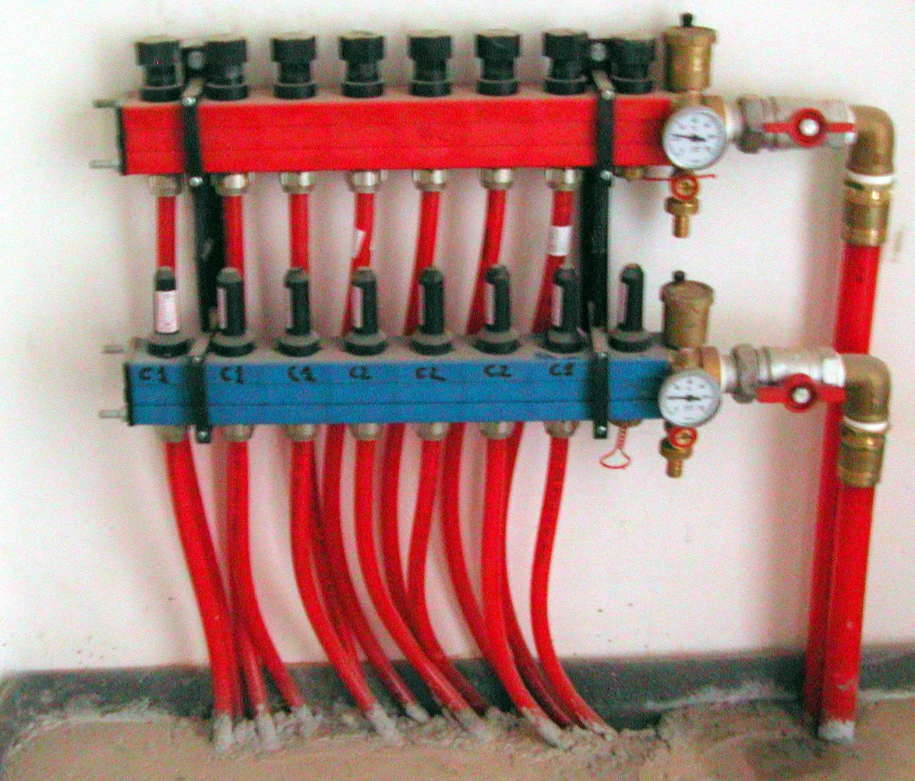 Verdeler van vloerverwarming met rode en blauwe leidingen en drukmeters